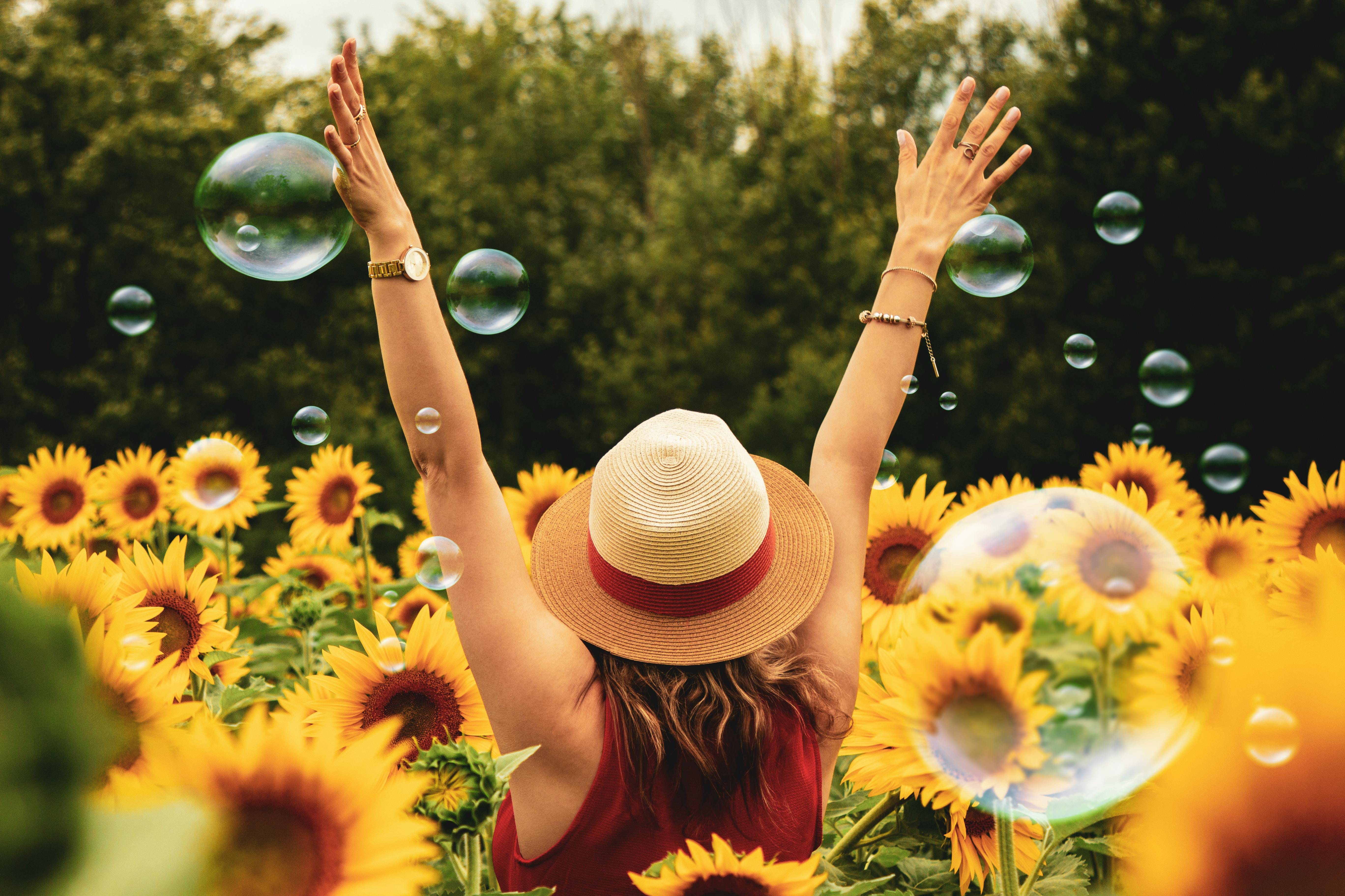 woman in field of sunflowers with arms raised in joy and bubbles floating nearby