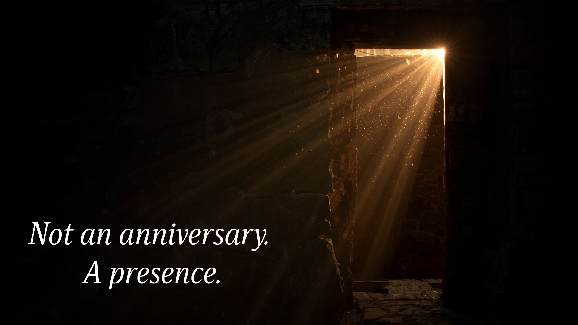 A dark stone chamber with a narrow doorway open to brilliant morning light. Rays of golden light stream through the opening, illuminating the rough stone walls and floor. The image conveys stillness and the sense of something present before you arrived.