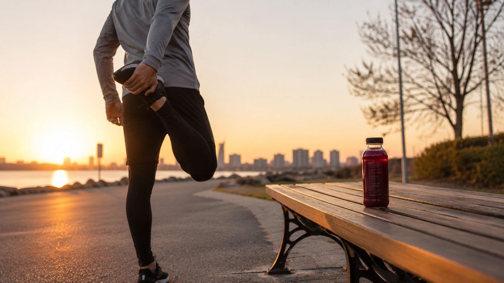 A runner stretches beside a park bench at sunrise while a bottle of dark red tart cherry juice rests nearby.